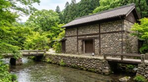 鹿児島県・妙見温泉の高級宿「妙見石原荘」にある、昭和初期の米倉庫を移築・再生した重厚な石造りの外観の客室棟「石蔵」。天降川沿いの緑に囲まれた歴史的建築イメージ