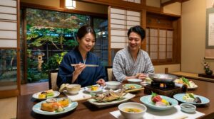黒川荘の完全個室のお食事処で、地産地消の創作懐石料理を楽しむ、浴衣姿のアジア人カップル。テーブルにはヤマメの塩焼きや肥後赤鶏のつみれ鍋など、熊本の旬の食材を使った美しい料理が並んでいる。美食とホスピタリティを強調。